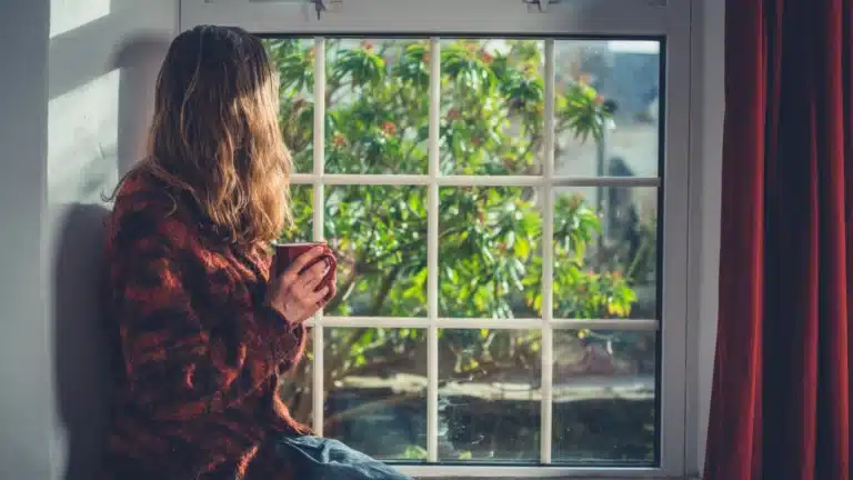 Person sitting by a window holding a mug and looking outside, symbolizing mindfulness, calm reflection, and natural wellness explored in medicinal mushroom safety guide.