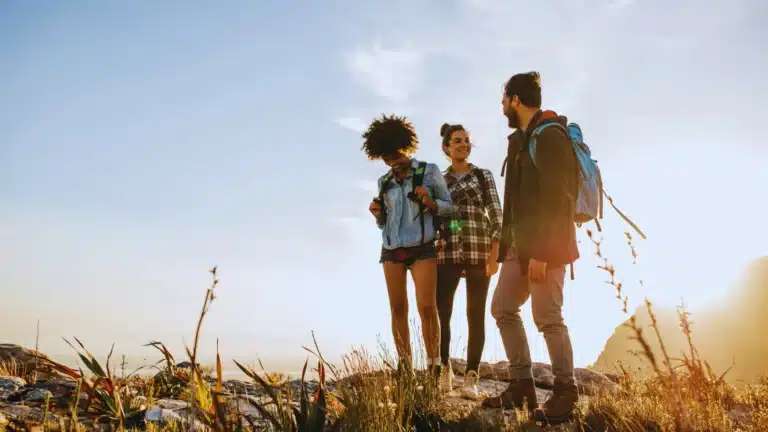 Three friends hiking outdoors on a sunny day, smiling and enjoying nature together