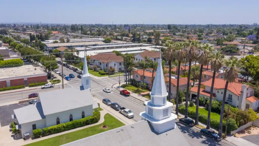 White church steeple at a street corner surrounded by palm trees and nearby homes in Pico Rivera, California.