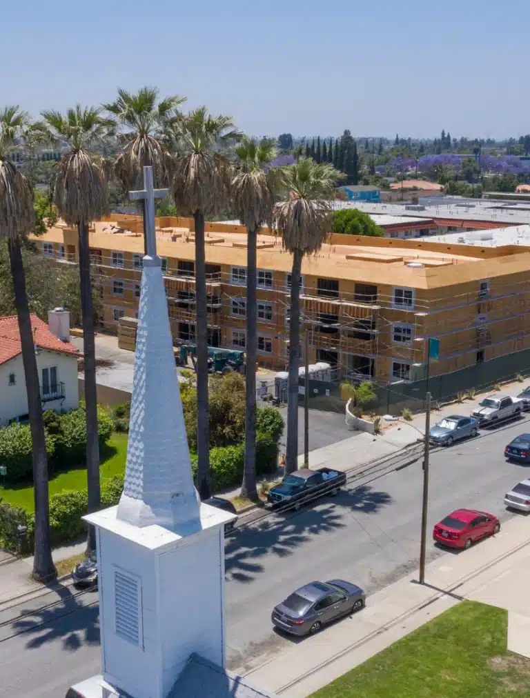 Aerial view of a church steeple and palm-lined street in Pico Rivera, California with apartments and parked cars.